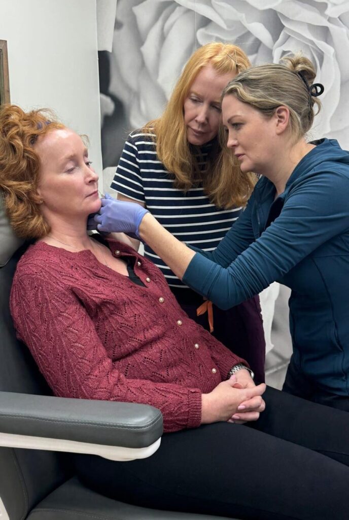 An instructor and trainee treating a seated model's neck during hands-on training